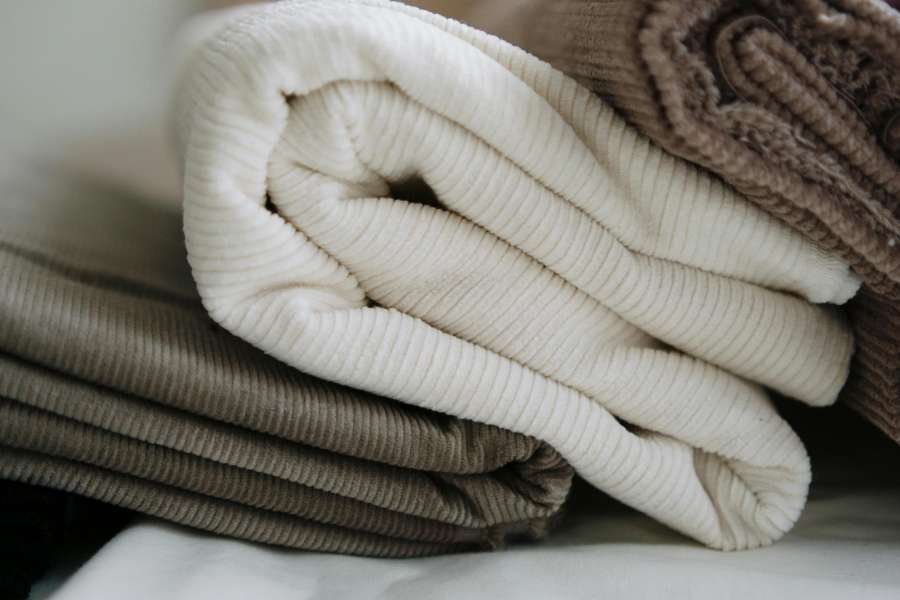A neatly stacked pile of soft use textiles and fabrics in cream, taupe, and brown corduroy tones.