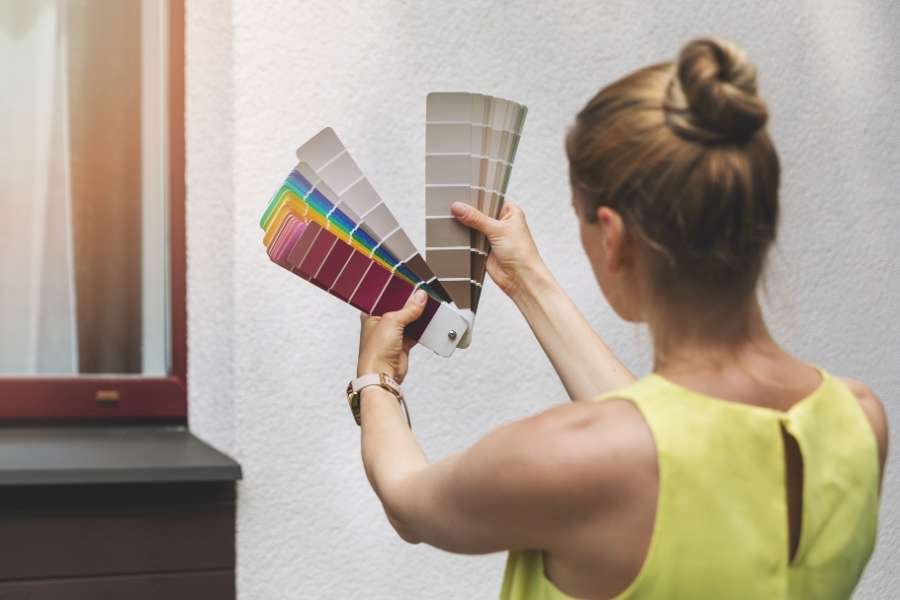 A woman holding colorful paint swatches against a textured wall to select exterior paint colors.